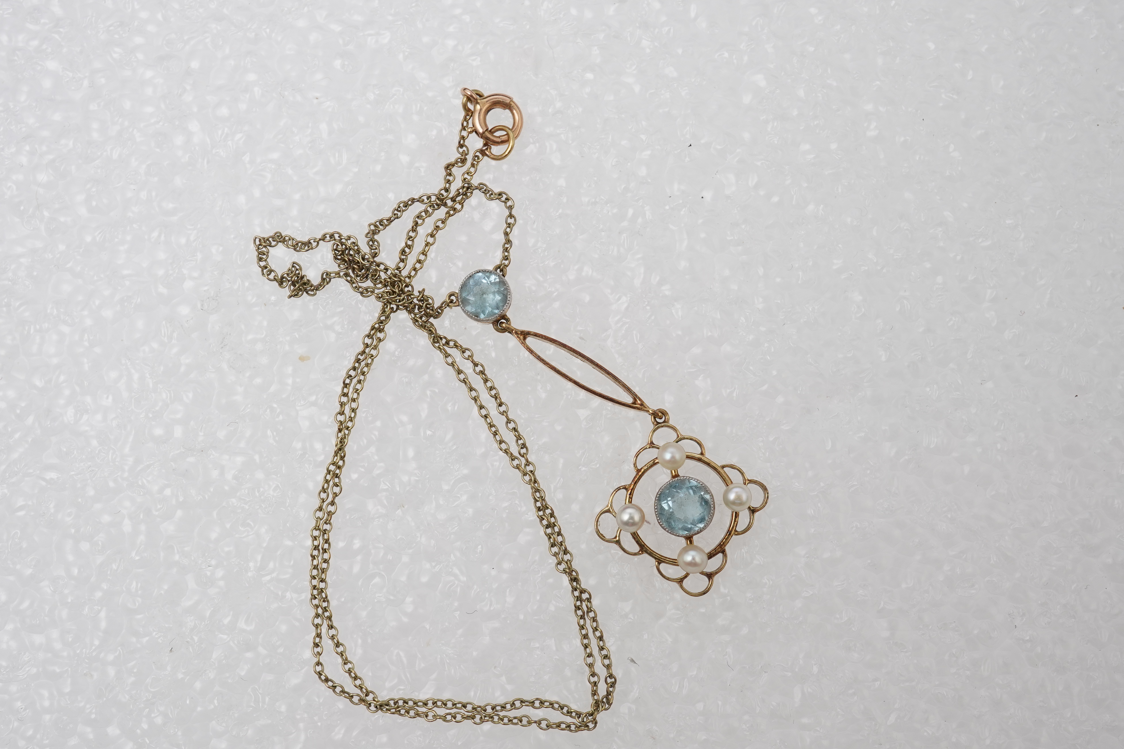 An Edwardian circular-cut aquamarine and seed pearl pendant, early 20th century, of foliate design, mounted in gold, pendant length 4cm, chain length 40cm, clasp stamped 15, gross weight approximately 3 grams, pearls unt